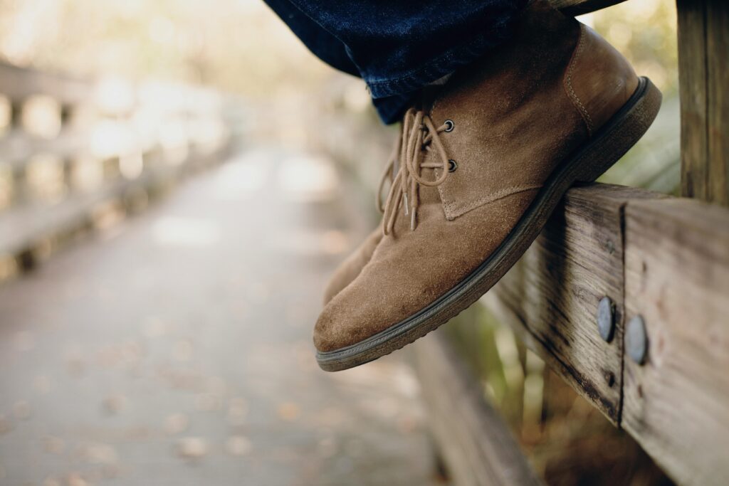 view of a mans brown suede shows. he is sitting on a fence.