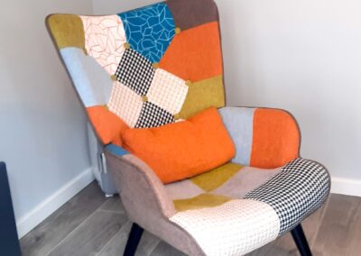 a comfy patchwork chair in Lindas counselling room with patches of all colours but mostly orange