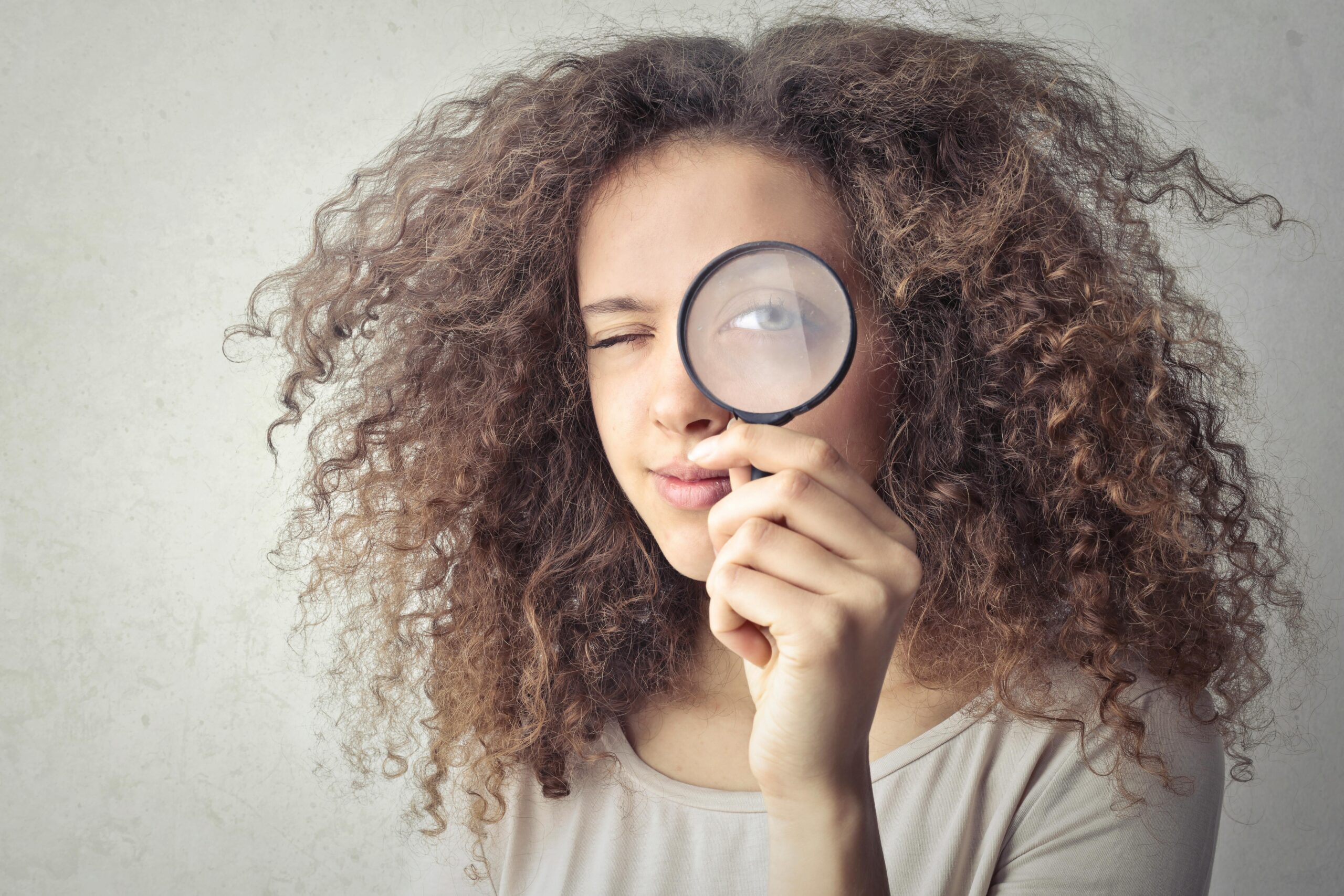 a woman with big hair holding a magnifying glass to her eye